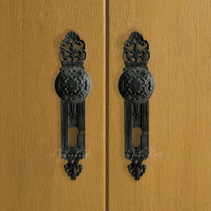 Puede incluir: Dos pomos de puerta negros ornamentados con agujeros de llave en una puerta de madera marrón claro.