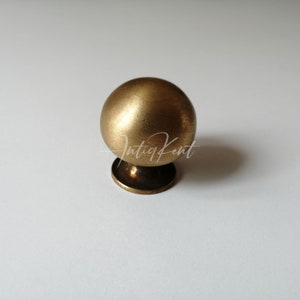 Może przedstawiać: Okrągły, szczotkowany mosiężny gałka do szafki z małą podstawą.