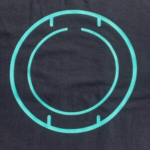 May include: A teal blue circle with a smaller teal blue circle inside, both with four small lines on the outer edge.
