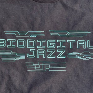 May include: Black t-shirt with a teal blue graphic design that says "Biodigital Jazz" with stylised circuit board lines.