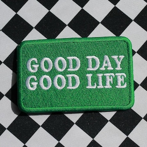 May include: Green embroidered patch with white text that reads "GOOD DAY GOOD LIFE" on a black and white chequered background.