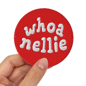 Könnte beinhalten: Ein runder, roter, gestickter Aufnäher mit den Worten "whoa nellie" in weißer, stilisierter Schrift. Der Aufnäher wird vor einem weißen Hintergrund präsentiert.
