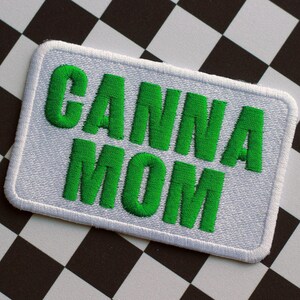 May include: Embroidered patch with the words "CANNA MOM" in bright green, on a white rectangular background with a white border. The background is a black and white chequered pattern.