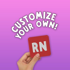 May include: A red fabric patch with white letters that spell "RN" on a pink background. The text "Customize Your Own!" is written in white letters on a pink background.