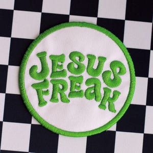 Könnte beinhalten: Ein weißer runder Patch mit grünem Rand. Die Worte "Jesus Freak" sind in Grün auf den Patch gestickt.