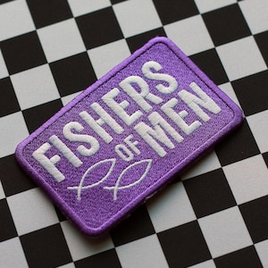 May include: A purple embroidered patch with the words "FISHERS OF MEN" in white, along with two fish symbols. The patch is rectangular and set against a black and white checkered background.