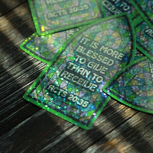 以下が含まれることがあります： 緑と青の虹色のステッカーに、「与えることは受けるよりも祝福される」というテキストと、「使徒の働き 20:35」という聖書の言葉が書かれています。