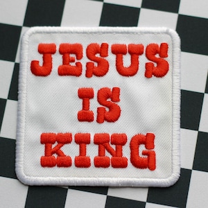 Pode incluir: Remendo branco com texto bordado em vermelho que diz "JESUS IS KING".