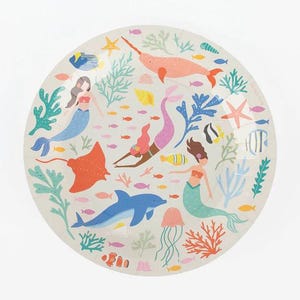 May include: Round paper plate with a whimsical under-the-sea design. The plate features mermaids, a narwhal, a dolphin, and various sea creatures in shades of pink, blue, orange, and yellow. Coral and seaweed accents complete the aquatic theme.
