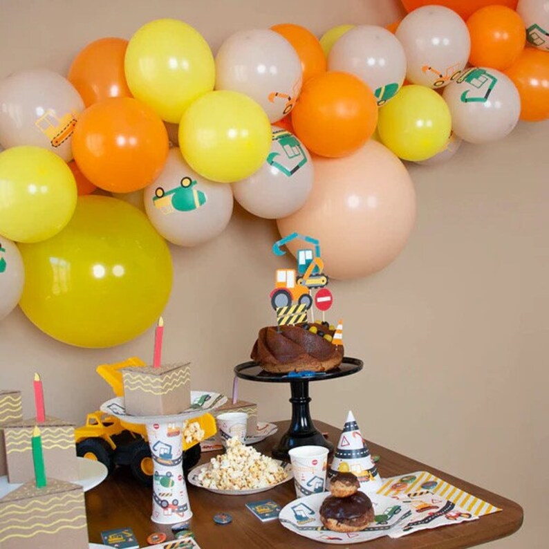 May include: A construction-themed birthday party with a chocolate cake decorated with construction vehicles, yellow and orange balloons, and construction-themed party supplies.