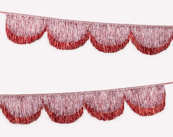 May include: Two strands of shimmering, scalloped garland. The top portion of each scallop is a light pink, transitioning to a vibrant red at the bottom. The garland is made of a metallic, fringed material, perfect for party decorations.