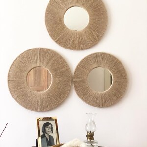 May include: Three round mirrors with a woven rope frame, hanging on a white wall. The mirrors are different sizes and are arranged in a triangular pattern.