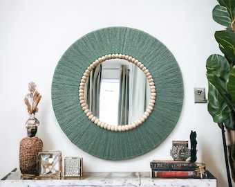 May include: A round green mirror with a wooden bead border. The mirror is hanging on a white wall above a wooden shelf with decorative items.