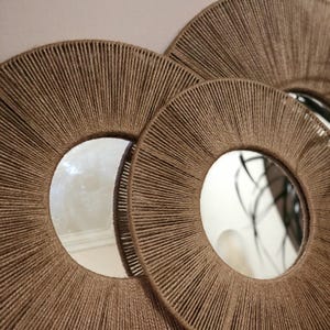 May include: Three round mirrors with a woven rope frame. The mirrors are nested inside each other, with the largest mirror in the back and the smallest mirror in the front.