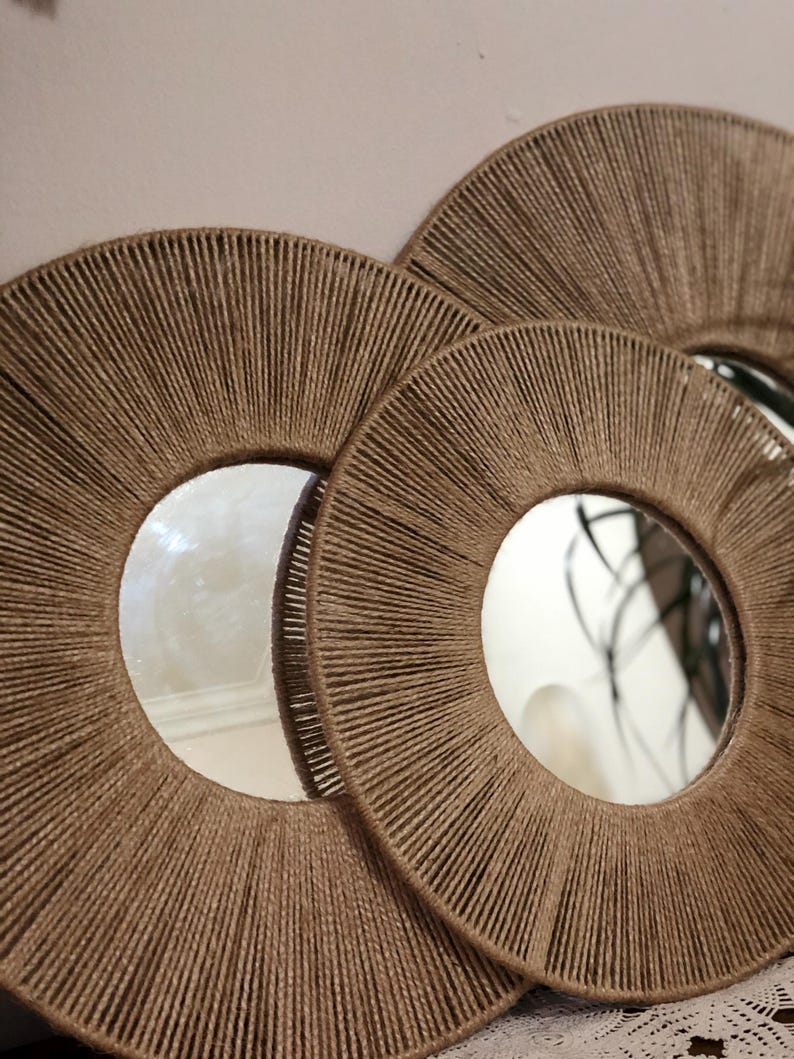 May include: Three round mirrors with a woven rope frame. The mirrors are nested inside each other, with the largest mirror in the back and the smallest mirror in the front.