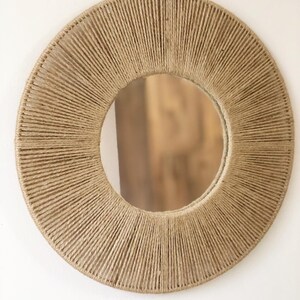 May include: A round mirror with a natural jute rope frame. The rope is woven in a circular pattern, creating a sunburst effect. The mirror is perfect for adding a touch of natural texture to any room.