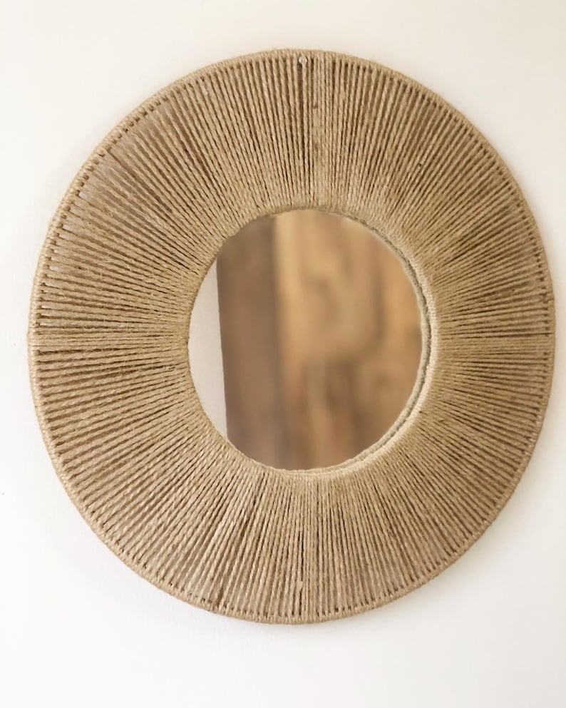 May include: A round mirror with a natural jute rope frame. The rope is woven in a circular pattern, creating a sunburst effect. The mirror is perfect for adding a touch of natural texture to any room.
