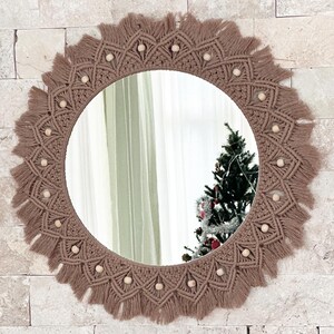 May include: A round mirror with a brown macrame frame and wooden beads. The frame has a fringe around the edge.