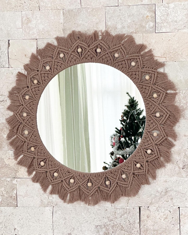 May include: A round mirror with a brown macrame frame and wooden beads. The frame has a fringe around the edge.