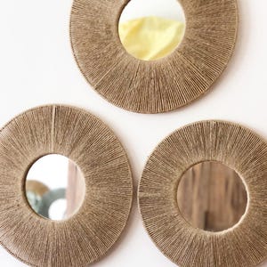 May include: Three round mirrors with a woven rope frame. The mirrors are different sizes and are arranged in a triangular pattern on a white wall.