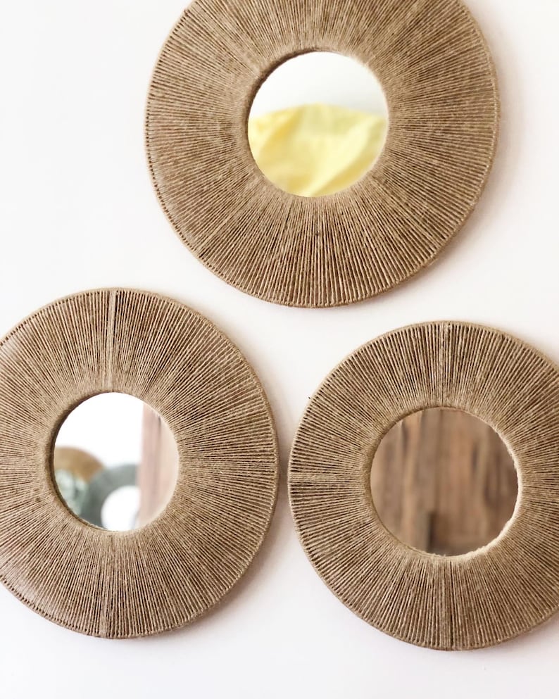 May include: Three round mirrors with a woven rope frame. The mirrors are different sizes and are arranged in a triangular pattern on a white wall.