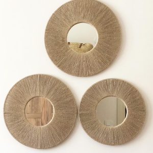 May include: Three round mirrors with a natural rope frame. The mirrors are different sizes and are arranged in a triangular pattern on a white wall.
