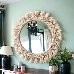 May include: A round mirror with a macrame frame and fringe. The frame is made of natural beige cotton rope and has a bohemian style.