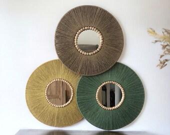 May include: Three round mirrors with woven rope frames and wooden bead accents. The mirrors are in shades of brown, yellow, and green. The mirrors are hanging on a white wall above a wooden dresser.