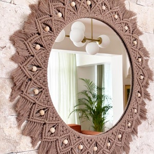 May include: A round mirror with a brown macrame frame and wooden beads. The frame has a fringe around the edge.