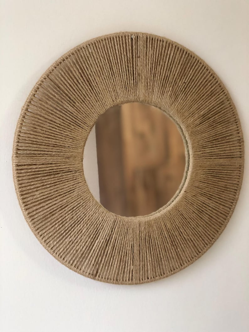 May include: A round mirror with a natural jute rope frame. The rope is woven in a circular pattern around the mirror.
