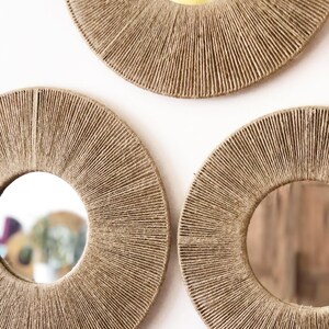 May include: Three round mirrors with a natural jute rope frame. The mirrors are different sizes and are arranged in a triangular pattern on a white background.