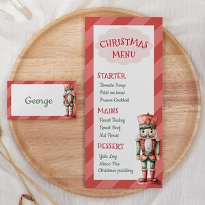 May include: A Christmas menu and place card on a wooden tray. The menu features a red and white striped design with a nutcracker illustration. The place card has the name "George" and a nutcracker image.