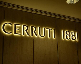以下が含まれることがあります： 「Cerruti 1881」と黒文字で書かれた金色の看板です。