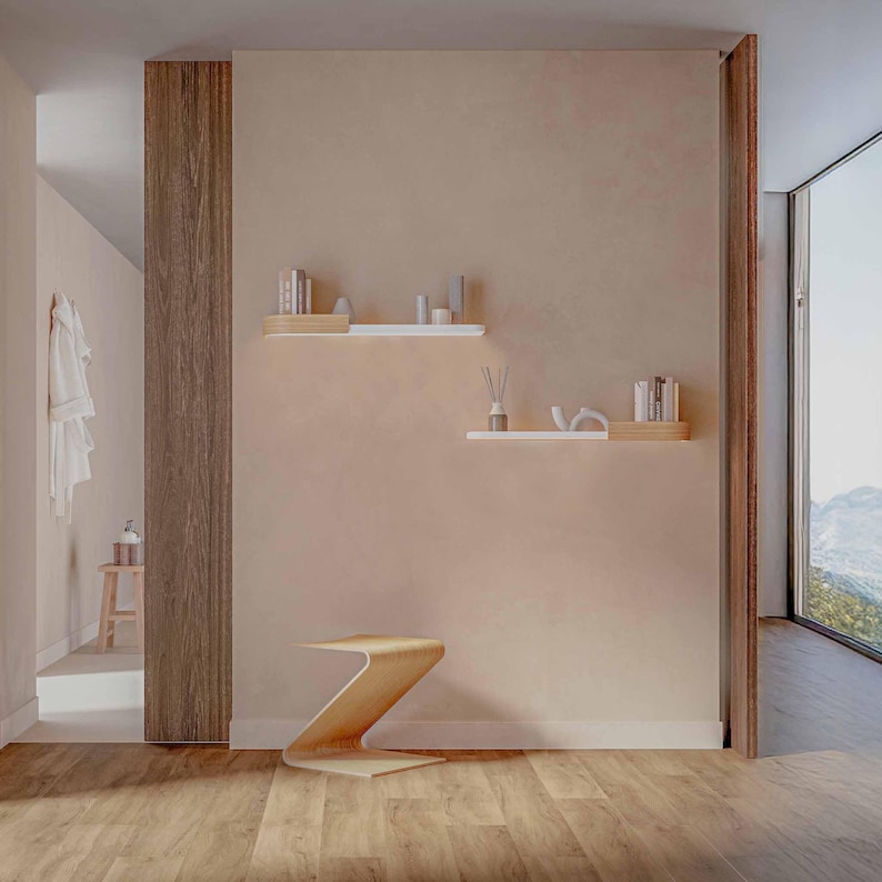 May include: A modern interior with a light brown wooden floor and a light brown wall. The room features a wooden Z-shaped side table, floating shelves with books and decorative items, and a large window with a mountain view.