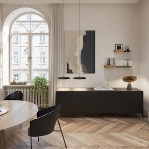 May include: An interior design scene featuring a black sideboard with drawers, a round dining table, and black chairs. A large arched window with a view of a building is visible. The room has a modern aesthetic with a neutral color palette.