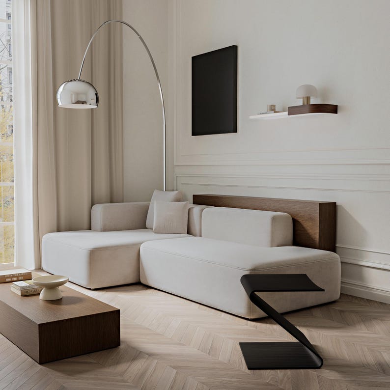 May include: A modern living room featuring a large, off-white sectional sofa with a wooden back. A chrome arc floor lamp with a spherical shade illuminates the space. A dark wood coffee table and a black side table complete the contemporary design.