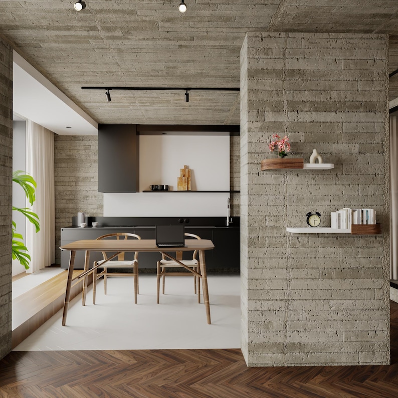 May include: A modern kitchen and dining area with a wooden table and chairs. A laptop sits on the table. The room features concrete walls, a black kitchen, and floating shelves with decor. A window with curtains is visible.