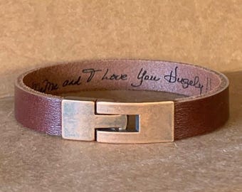 May include: A brown leather bracelet with a copper clasp. The bracelet has the words "Love me and I love you hugely" written on the inside.