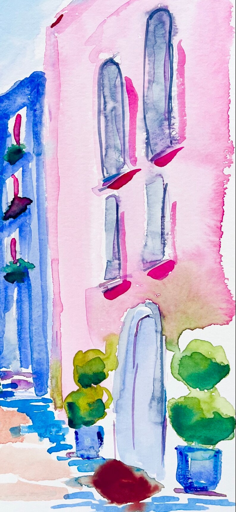 以下が含まれることがあります： ピンクの建物に青い窓と青いドアが描かれた水彩画。建物の前に、鉢植えの緑の茂みが2つある。