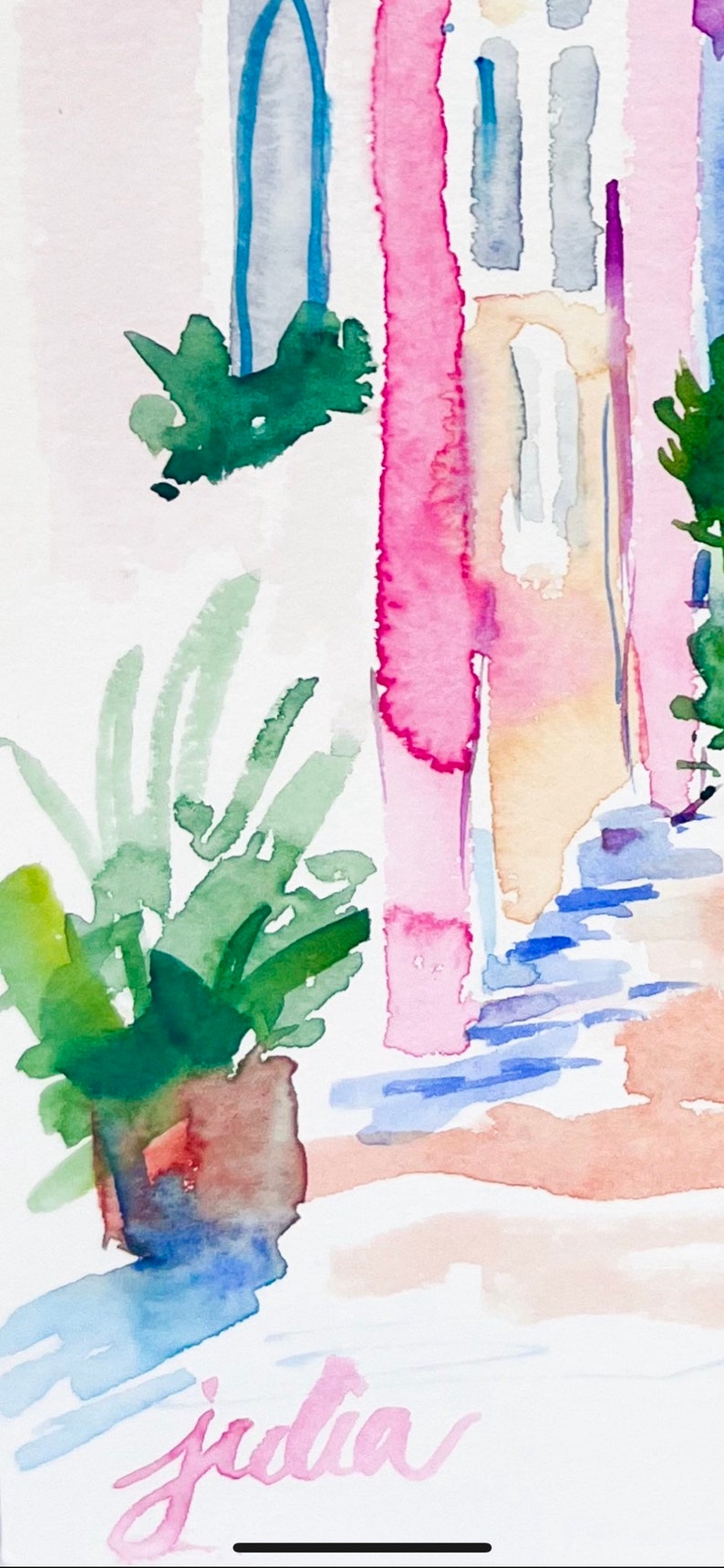 以下が含まれることがあります： ピンクの建物を描いた水彩画。窓は青と黄色。手前に緑の植物がある。右下に「julia」という署名がある。