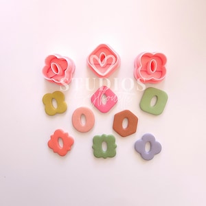 May include: A collection of pink cookie cutters in various floral and geometric shapes, alongside similarly shaped cookies in shades of green, pink, and brown. The image includes the text "STUDIOS by Honore".