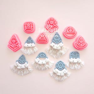 May include: Pink polymer clay earring cutters and several pairs of handmade earrings with blue and white macrame details. The earrings have a geometric design with a fringe of white macrame. The text "Silhouette Studios" is visible.