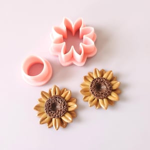 Op de afbeelding: Een set van drie roze plastic koekjesuitstekers in de vorm van zonnebloemen. De uitstekers worden gebruikt om eetbare decoraties voor taarten en andere gebakjes te maken.