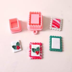 Peut inclure: Emporte-pièces carrés roses et plusieurs petits biscuits carrés décorés. Les biscuits ont des centres blancs avec des accents rouges et verts, dont des feuilles de houx et des baies, et des bordures rayées rouges et blanches.