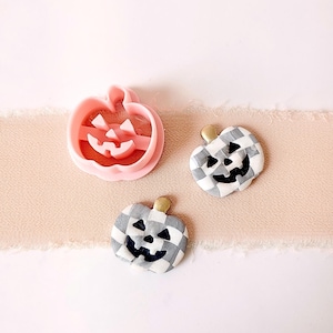 May include: Two white and black checkered pumpkin shaped ornaments with black jack-o-lantern faces and a pink plastic pumpkin cookie cutter.