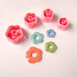 May include: Set of seven pink and pastel colored flower-shaped cookie cutters and fondant cutters. The cutters are in various sizes and have a hole in the center.