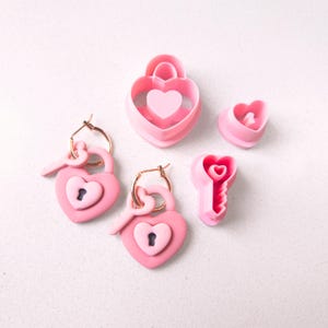 May include: Pink heart-shaped lock and key cookie cutters. The lock cutter has a small heart inside and the key cutter has a small heart on the top.