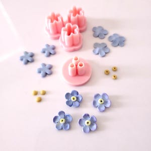 May include: A set of pink and purple fondant flower cutters and molds, along with blue and yellow fondant flowers and gold beads. The set includes three flower cutters, a flower mold, and a variety of pre-made flowers.