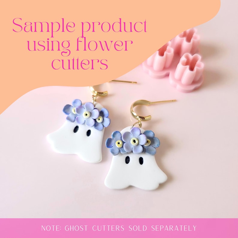 May include: A pair of white ghost-shaped earrings with a purple flower crown. The earrings are made of polymer clay and have gold hoops. The image also shows a pink flower cutter.