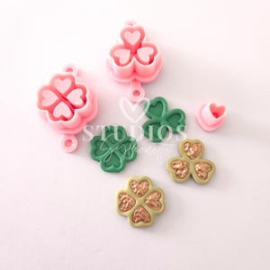 May include: Four-leaf clover shaped molds for crafting, two are pink and two are green. There are also two gold four-leaf clovers with a textured surface.